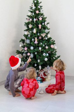 Three children in pajamas decorating a Christmas tree. Christmas Tradition.