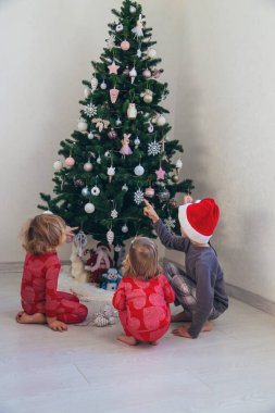 Three children in pajamas decorating a Christmas tree. Christmas Tradition.