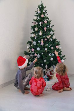 Three children in pajamas decorating a Christmas tree. Christmas Tradition.