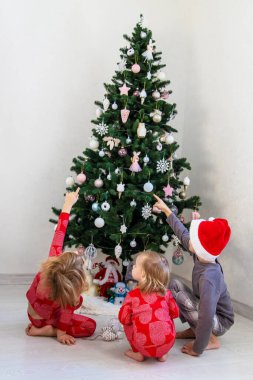 Three children in pajamas decorating a Christmas tree. Christmas Tradition.