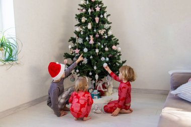 Three children in pajamas decorating a Christmas tree. Christmas Tradition.