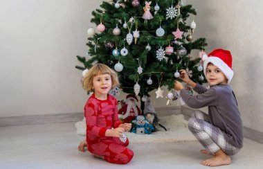 Three children in pajamas decorating a Christmas tree. Christmas Tradition.