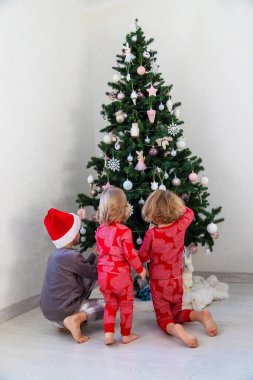 Three children in pajamas decorating a Christmas tree. Christmas Tradition.