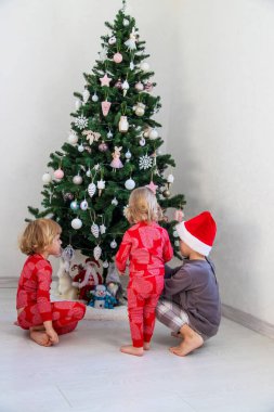 Three children in pajamas decorating a Christmas tree. Christmas Tradition.