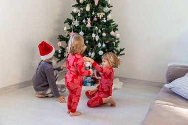 Three children in pajamas decorating a Christmas tree. Christmas Tradition.