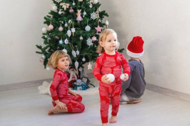 Three children in pajamas decorating a Christmas tree. Christmas Tradition.