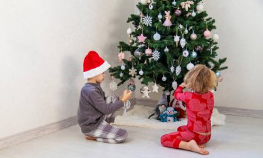 Three children in pajamas decorating a Christmas tree. Christmas Tradition.