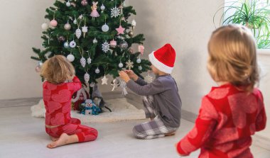 Three children in pajamas decorating a Christmas tree. Christmas Tradition.