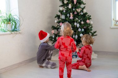 Three children in pajamas decorating a Christmas tree. Christmas Tradition.