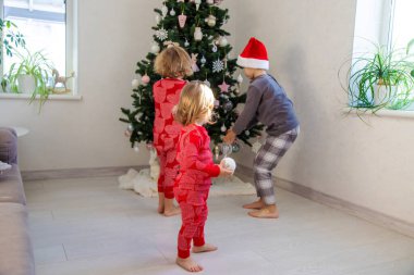 Three children in pajamas decorating a Christmas tree. Christmas Tradition.