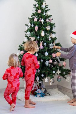 Three children in pajamas decorating a Christmas tree. Christmas Tradition.