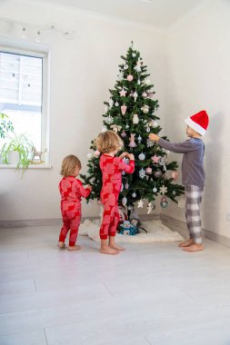 Three children in pajamas decorating a Christmas tree. Christmas Tradition.