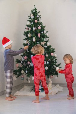Three children in pajamas decorating a Christmas tree. Christmas Tradition.