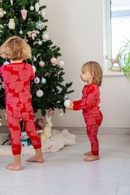 Three children in pajamas decorating a Christmas tree. Christmas Tradition.