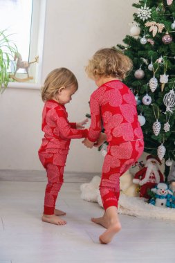 Three children in pajamas decorating a Christmas tree. Christmas Tradition.