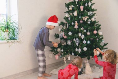 Three children in pajamas decorating a Christmas tree. Christmas Tradition.