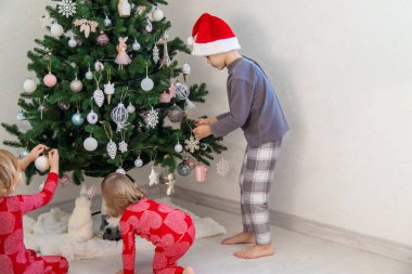 Three children in pajamas decorating a Christmas tree. Christmas Tradition.
