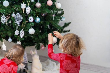 Three children in pajamas decorating a Christmas tree. Christmas Tradition.