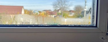 Güneşli bir günde evin ve ağacın bulanık görünümlü penceresine damlacıklar konur.