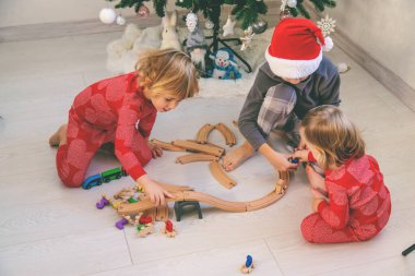 Üç çocuk evdeki Noel ağacının yanında tahta bir oyuncak treniyle oynuyor..