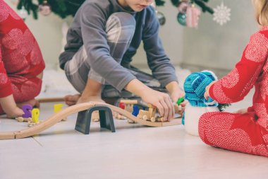 Üç çocuk evdeki Noel ağacının yanında tahta bir oyuncak treniyle oynuyor..