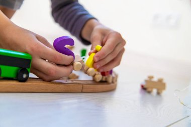 Çocuk, parlak bir zeminde renkli harflerle tahta bir oyuncak treniyle oynuyor.