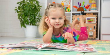 Parlak elbiseli küçük bir kız evde renkli bir paspasın üzerinde oyun oynuyor ve öğreniyor.