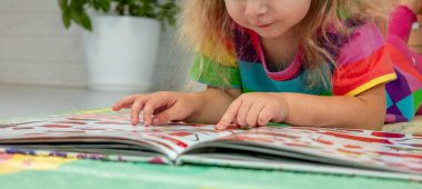 Parlak elbiseli küçük bir kız evde renkli bir paspasın üzerinde oyun oynuyor ve öğreniyor.