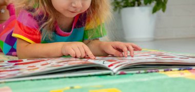 Parlak elbiseli küçük bir kız evde renkli bir paspasın üzerinde oyun oynuyor ve öğreniyor.