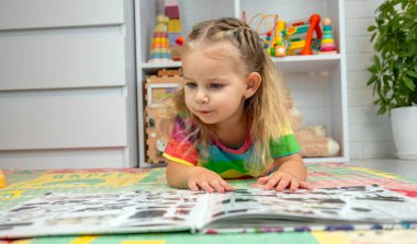 Parlak elbiseli küçük bir kız evde renkli bir paspasın üzerinde oyun oynuyor ve öğreniyor.