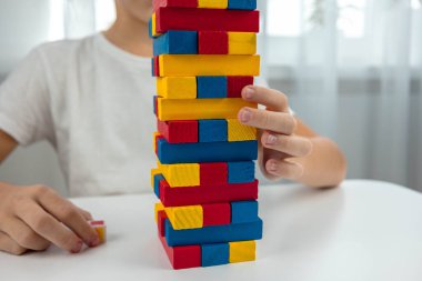 Jenga masa oyunu oynayan çocuk, dikkatlice renkli bir tahta bloğu kuleden çekiyor..
