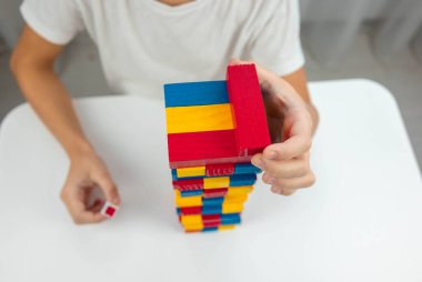 Jenga masa oyunu oynayan çocuk, dikkatlice renkli bir tahta bloğu kuleden çekiyor..