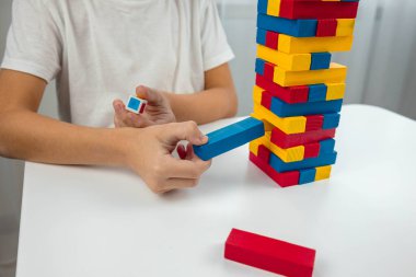 Jenga masa oyunu oynayan çocuk, dikkatlice renkli bir tahta bloğu kuleden çekiyor..