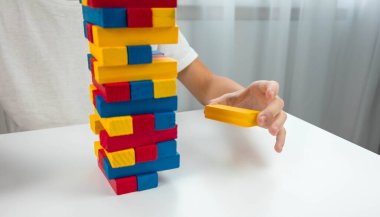 Jenga masa oyunu oynayan çocuk, dikkatlice renkli bir tahta bloğu kuleden çekiyor..