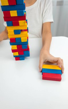 Jenga masa oyunu oynayan çocuk, dikkatlice renkli bir tahta bloğu kuleden çekiyor..