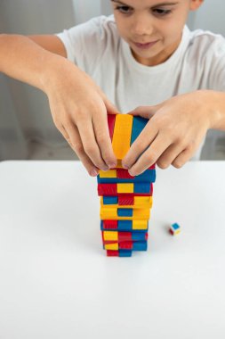 Jenga masa oyunu oynayan çocuk, dikkatlice renkli bir tahta bloğu kuleden çekiyor..