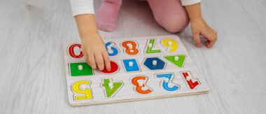 Yeni yürümeye başlayan kız, tahta bir eğitim bulmacasıyla oynuyor ve evde yerde şekiller ayırıyor.