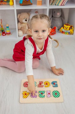 Yeni yürümeye başlayan kız, tahta bir eğitim bulmacasıyla oynuyor ve evde yerde şekiller ayırıyor.