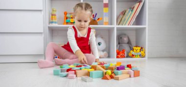 Küçük kız yerde renkli ahşap bloklar olan bir kule inşa ediyor.