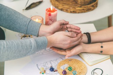 Falcılık oturumunda astrolojik çizelge üzerinde rün taşlarını tutan iki çift el görülüyor..