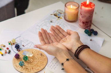 Arka planda astrolojik çizelgeler olan bir dizi rün taşı tutan eller. Falcı..