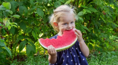 Mutlu küçük kız yeşil bir bahçenin arka planında sulu bir karpuz yiyor..