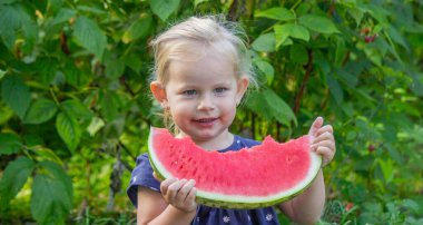 Mutlu küçük kız yeşil bir bahçenin arka planında sulu bir karpuz yiyor..