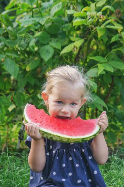 Mutlu küçük kız yeşil bir bahçenin arka planında sulu bir karpuz yiyor..