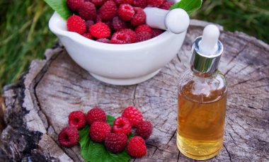 Şişe içinde ahududu esanslı yağ ve ahşap bir kütükte taze böğürtlen