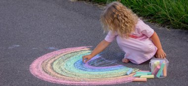 Küçük kız yazın asfalta renkli tebeşirle parlak bir gökkuşağı çiziyor.
