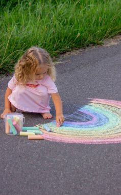 Küçük kız yazın asfalta renkli tebeşirle parlak bir gökkuşağı çiziyor.