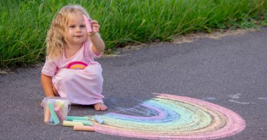 Küçük kız yazın asfalta renkli tebeşirle parlak bir gökkuşağı çiziyor.