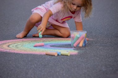 Küçük kız yazın asfalta renkli tebeşirle parlak bir gökkuşağı çiziyor.