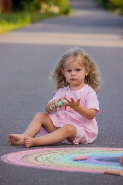 Küçük kız yazın asfalta renkli tebeşirle parlak bir gökkuşağı çiziyor.